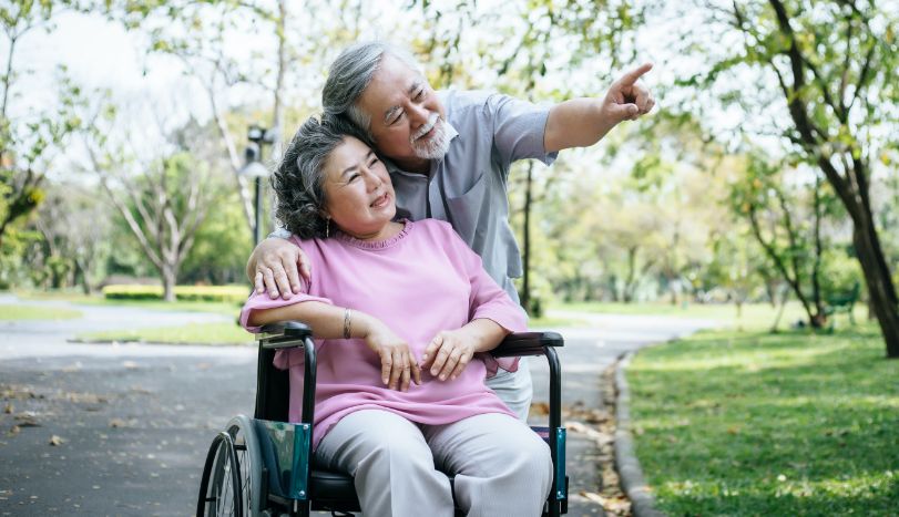 Senior man holding his disabled elderly wife in a wheelchair during spring in park