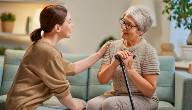Young woman patting elderly woman on couch in home