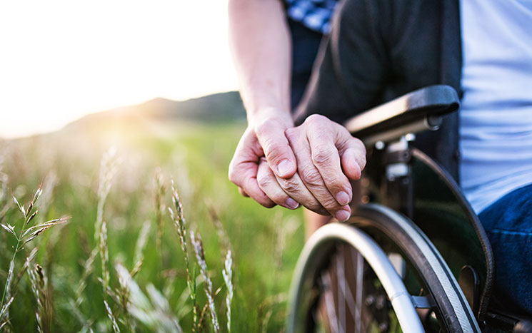 Son holding fathers hand in wheelchair at plains during sunset