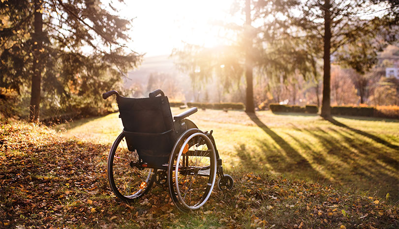 Empty wheelchair on grass in park setting with sunset in background