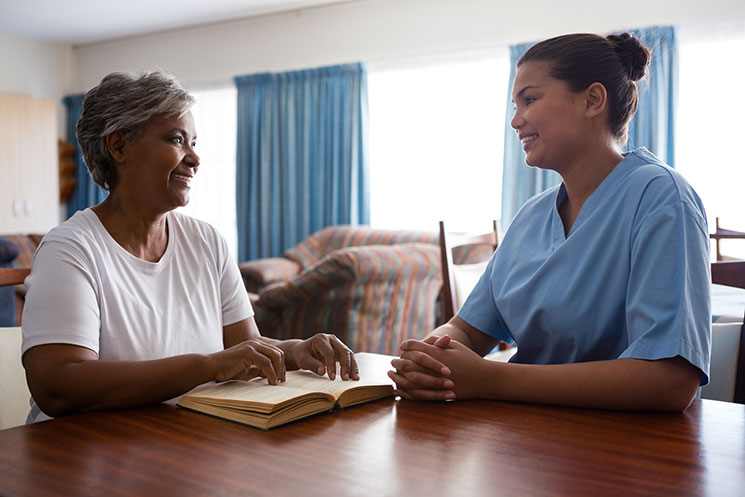 Hospice nurse talking to hospice patient in home with book