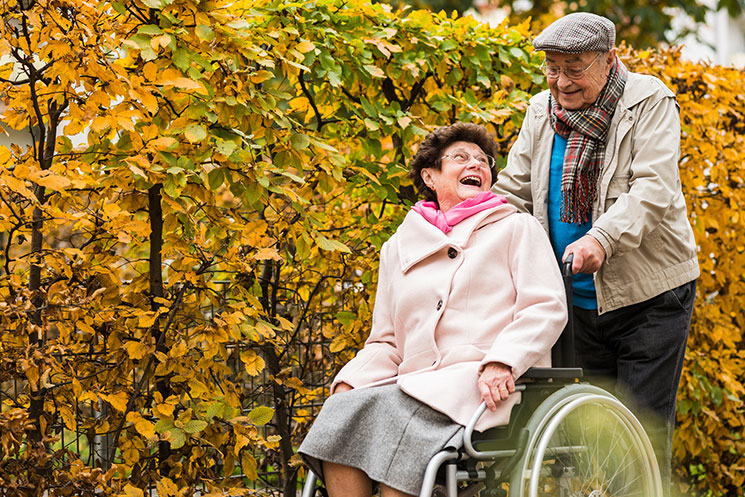 Senior man pushing elderly wife in wheelchair at park during daytime