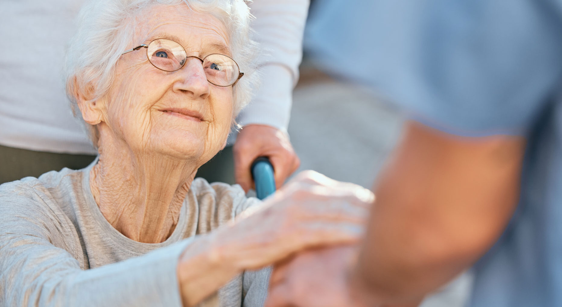 Elder hospice patient in a wheelchair smiling and holding the hand of an out of frame hospice care staff