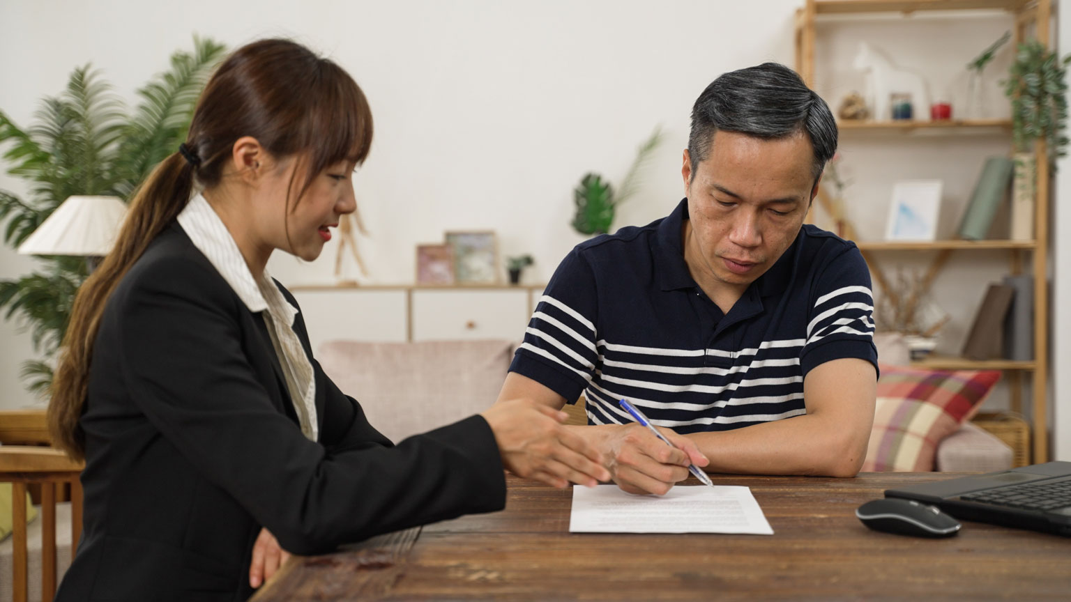 An elderly gentleman signing papers in front of a legal counsel