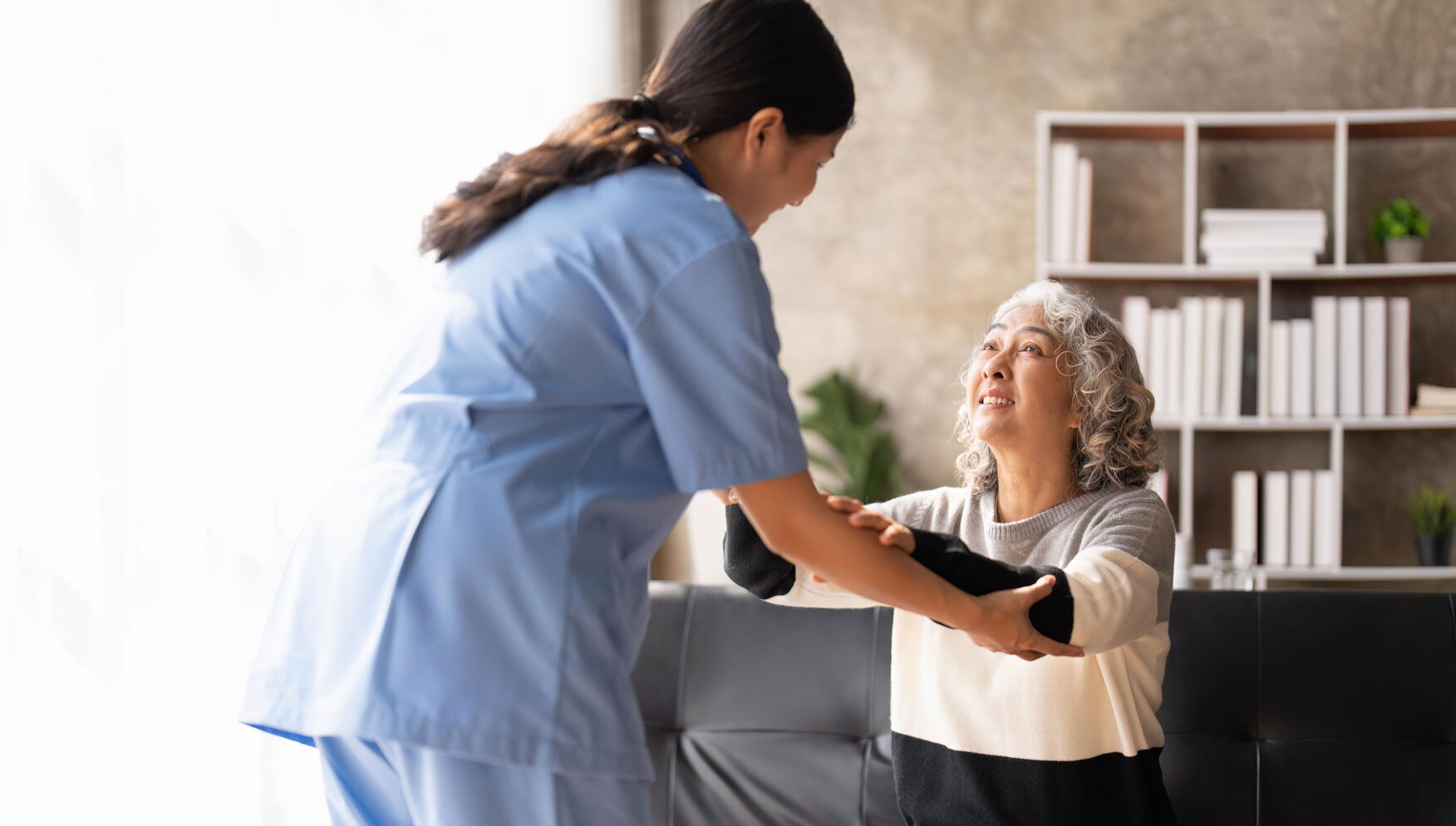 Home health care nurse in blue scrubs assisting an elderly patient