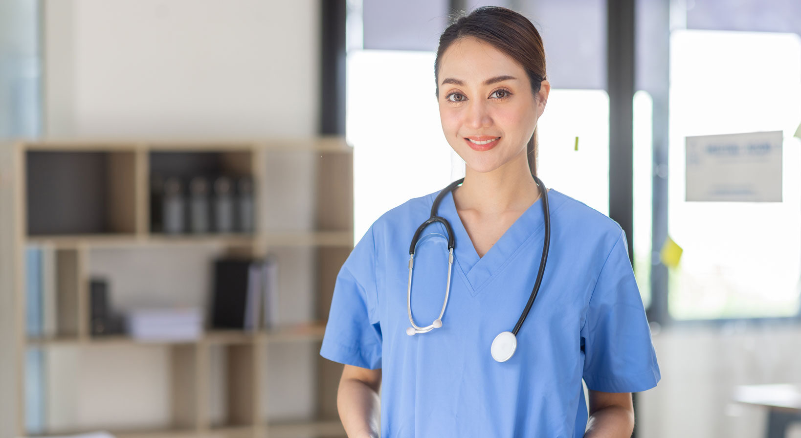 Image of a hospice care nurse in blue scrubs with a stethoscope draped on neck, smiling confidently