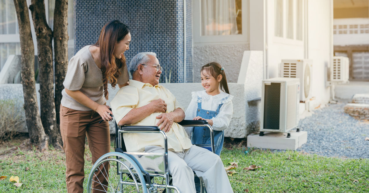 Image of a woman and a little girl smiling and interacting with an elderly in a wheelchair outdoors