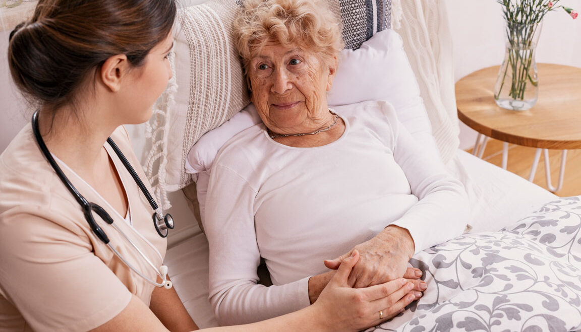Image of an elderly person on a bed holding hands with a hospice carer