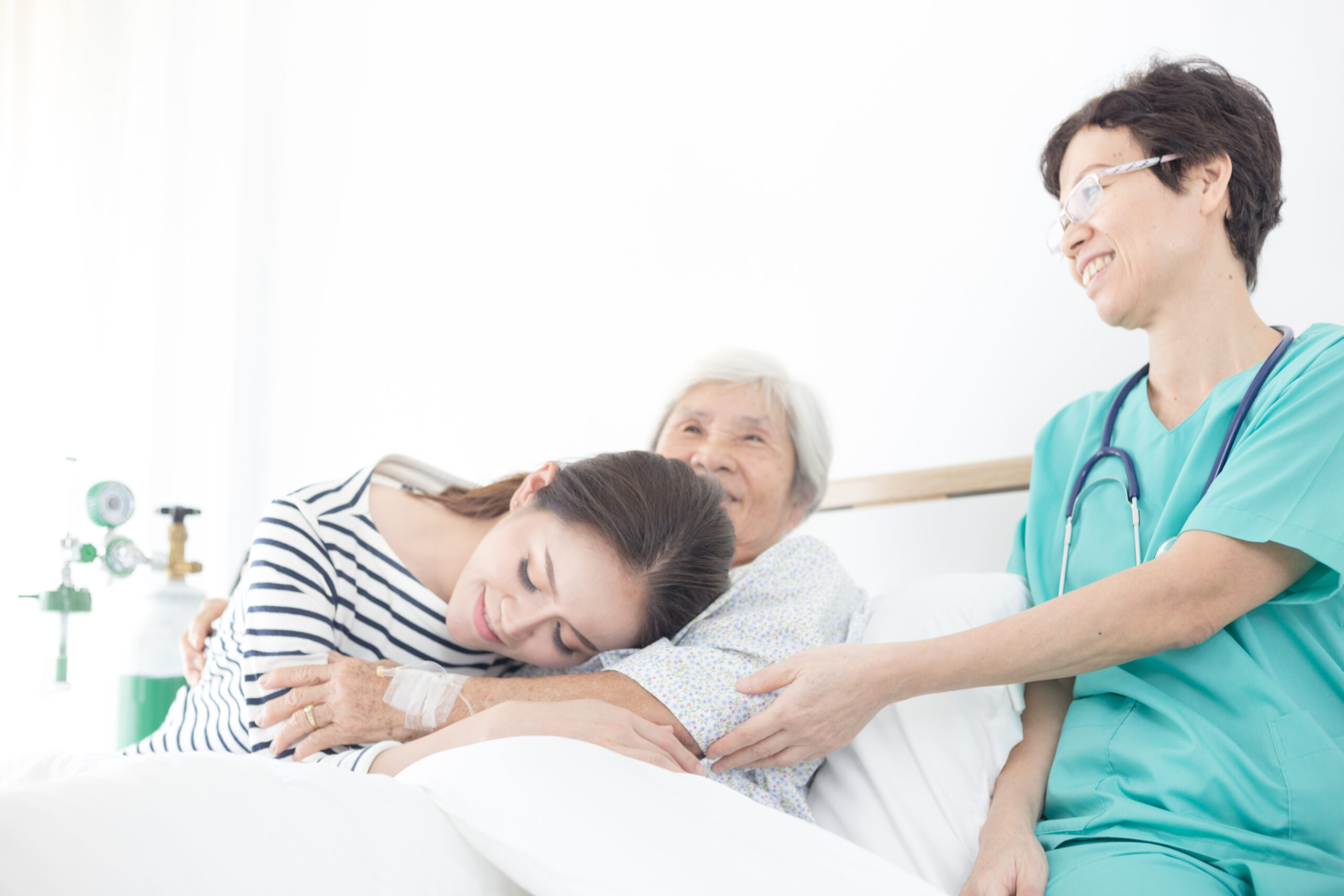Elderly female patient smiling in bed being comforted by her daughter and a female doctor