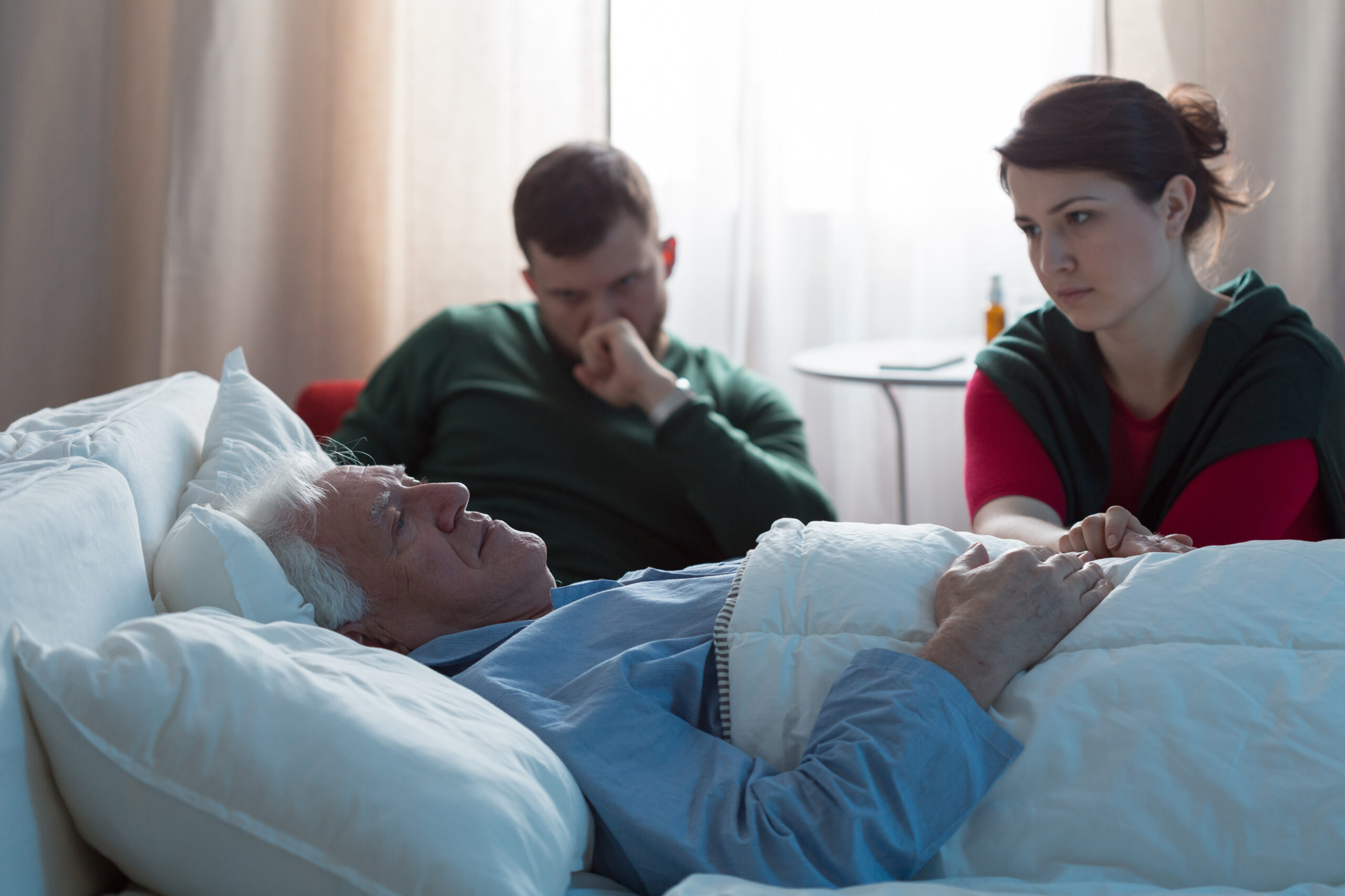 Elderly male patient in bed while his son and daughter are seated near him 